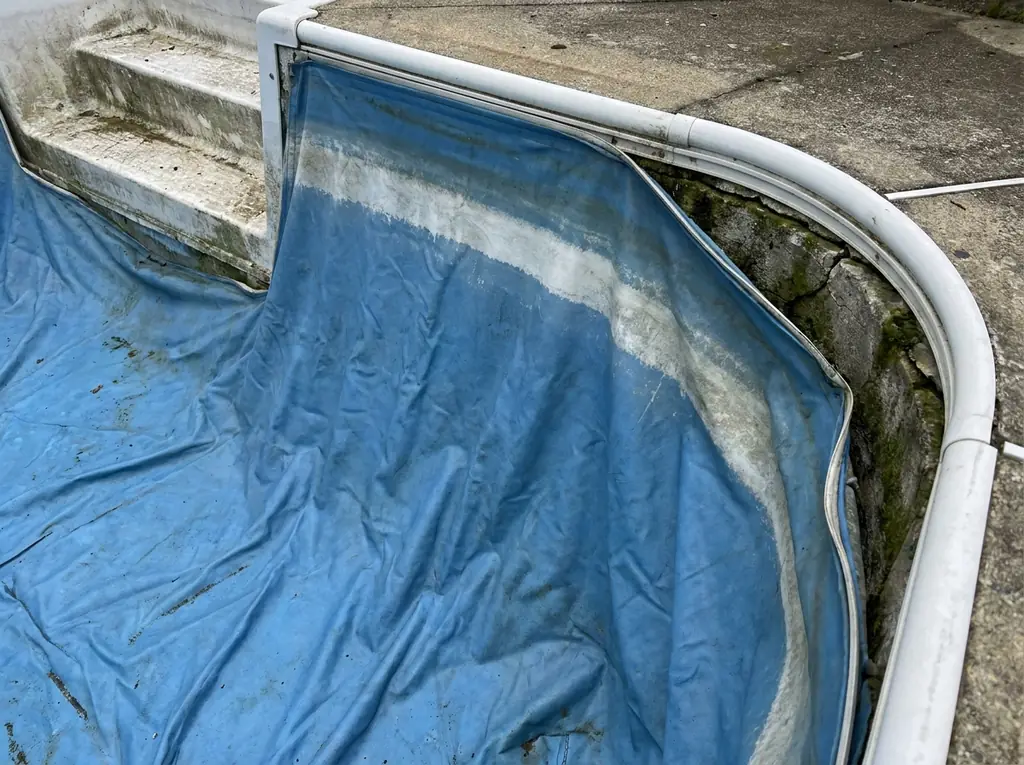 Close-up of a failing vinyl pool liner showing a wrinkle and a bleached waterline near the steps